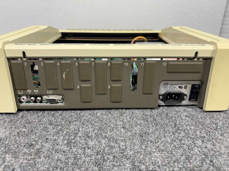 Back view of the Apple IIe computer showing ports and vents, placed on a carpeted table surface